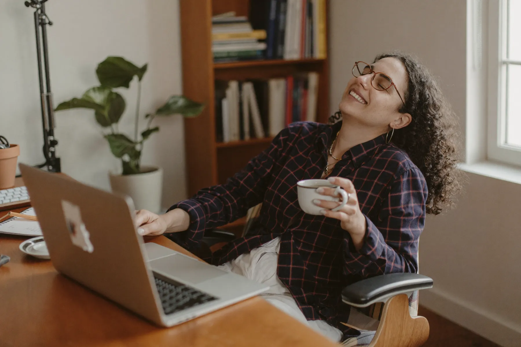 Eine Webentwicklerin arbeitet im Homeoffice am Laptop, neben ihr steht eine Tasse Tee.